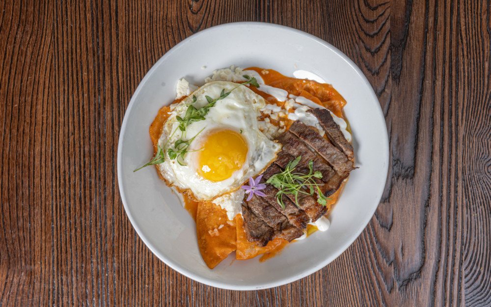 Smoked piranha, red sauce, queso fresco, Mexican cream, fried egg, cilantro on super crispy corn totopos.