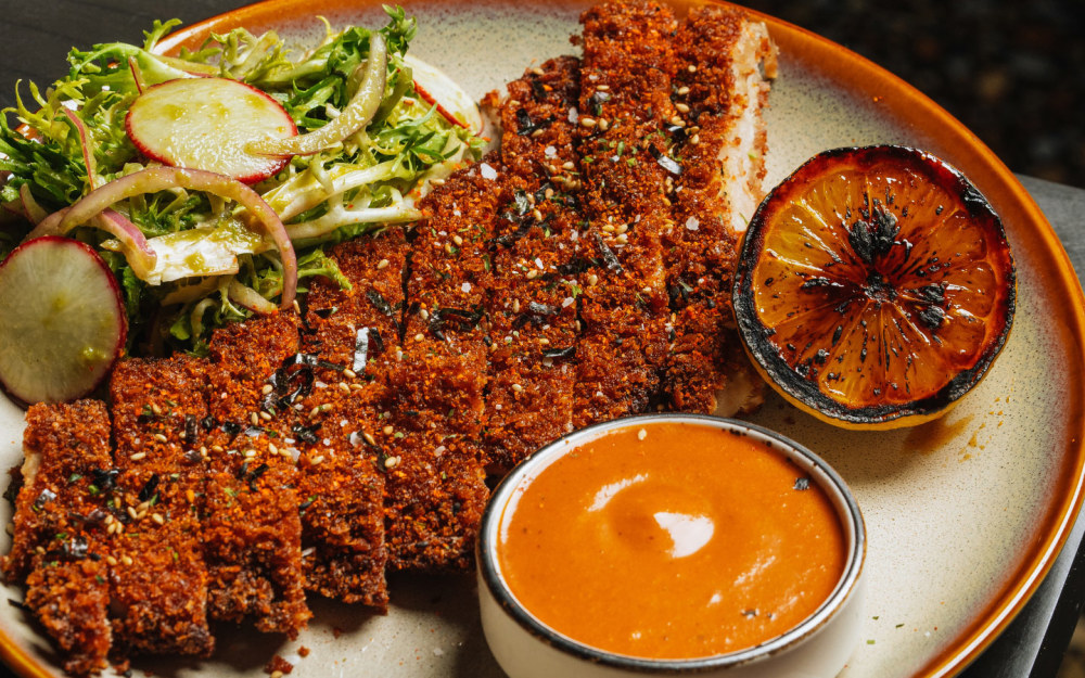 Deliciosamente crujiente Katsu de cerdo con costra de panko Sazon Completa, servido con ensalada friseé y arroz blanco.