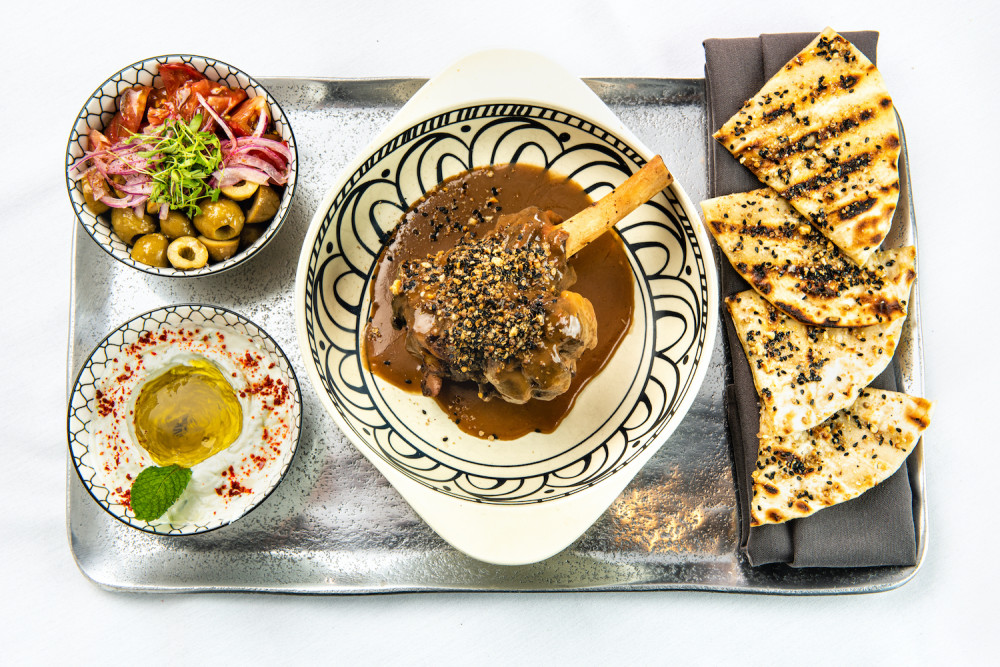 A perna de cordeiro da Tur Kitchen é servida com Tzatziki, Tomate Heirloom, Cebola, Dukkah e Pão Achatado