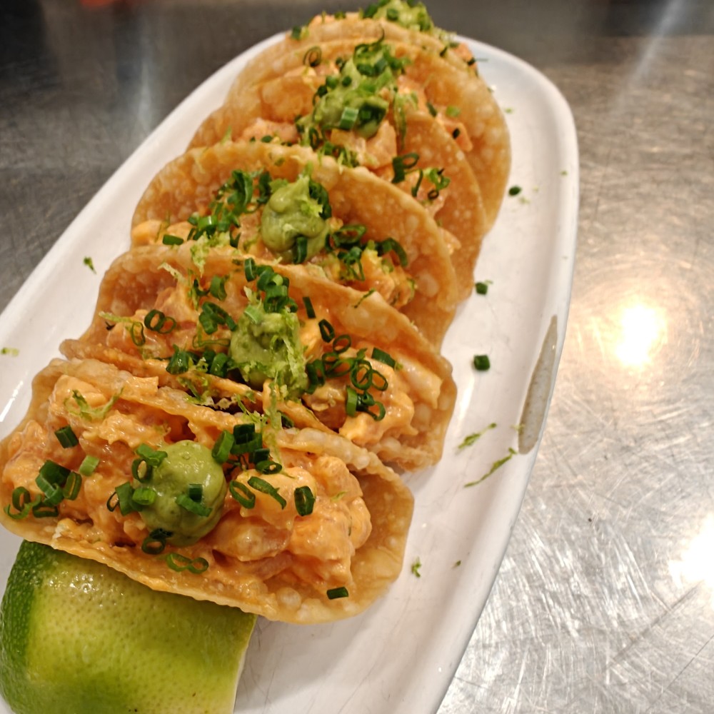 Salmão curado da Patagônia misturado com maionese aioli coreana picante, colocado em uma casca de wonton crocante, coberto com abacate cremoso e decorado com raspas de limão