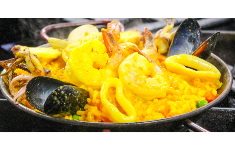 Paellita de Mariscos: arroz a la española con camarones, pulpo, almejas, mejillones y calamares; cubierto con zanahorias, guisantes y pimiento rojo asado.