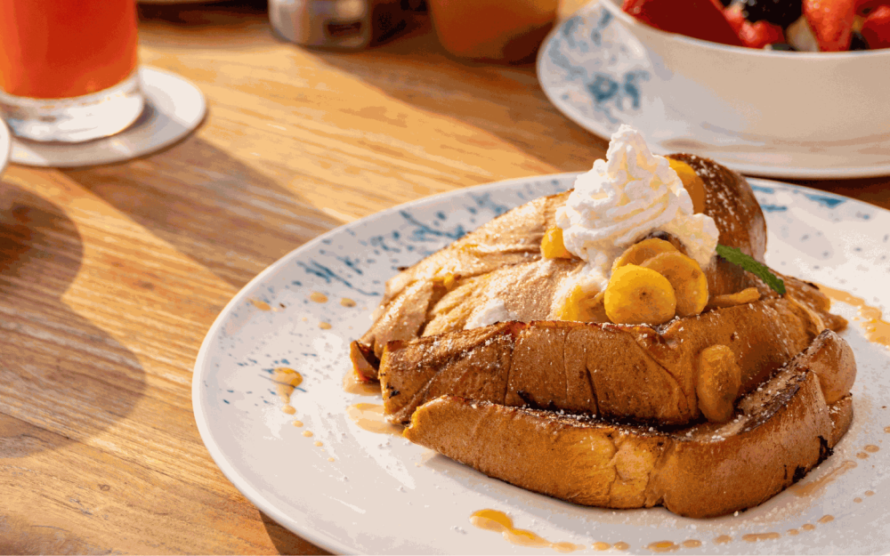 Delight in the Banana Foster French Toast: Brioche, caramelized bananas, whipped cream, maple syrup. Breakfast reimagined.