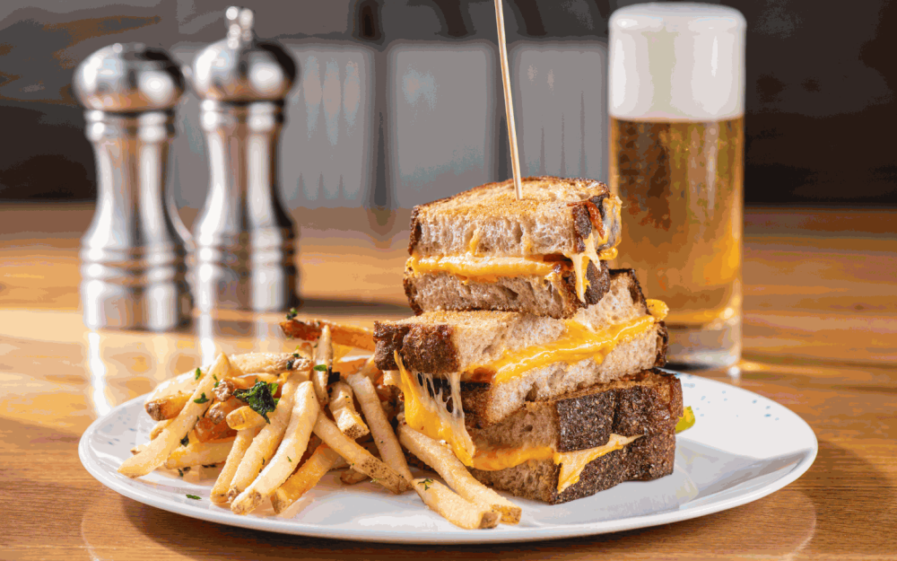 The Grilled Cheese is described as "Melty Goodness" made with aged cheddar, gouda, American and a side of herb fries.