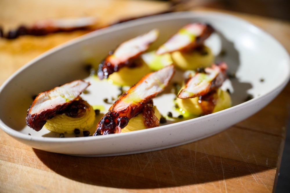 Polvo grelhado com pasta de fava Santorini, cebolas caramelizadas, alcaparras crocantes e óleo de endro.