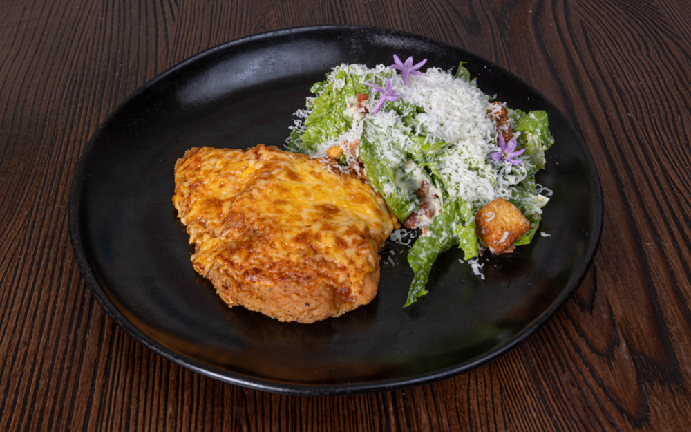 Milanesa de pollo con salsa diabla, chihuahua y queso manchego Crust y ensalada César como acompañamiento.