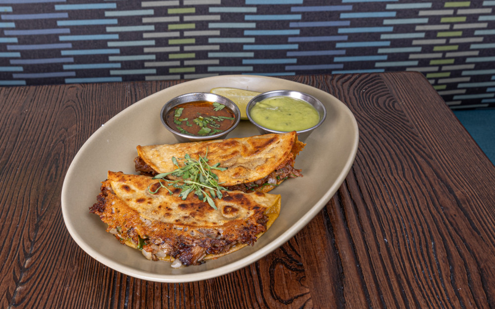 Birria brisket, chihuahua and manchego cheese crust, white onions, cilantro, clad de brio, avocado and zucchini sauce.