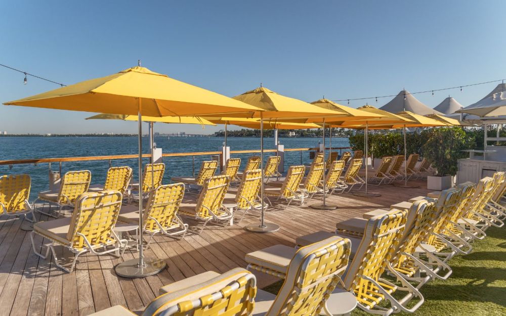 Signature waterfront sun deck at The Standard Spa, Miami Beach, with yellow umbrellas, lounge chairs, and Biscayne Bay views.
