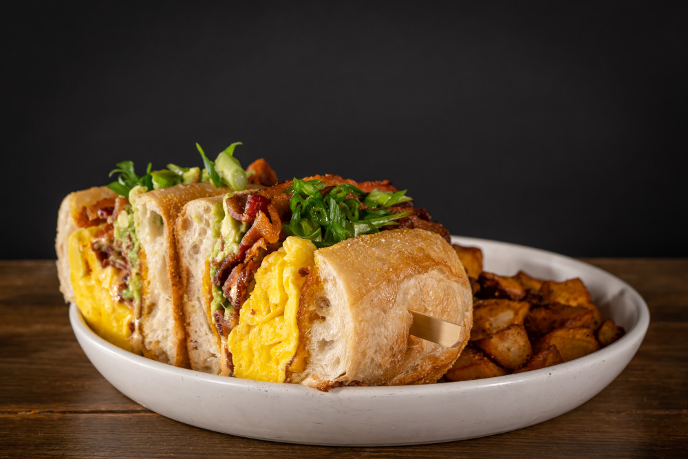 Americano Breakfast Sandwich: Fluffy Scrambled Eggs, Cheddar and Provolone Cheeses, Ham, Griddled Thick Cut White Bread & Breakfast Potatoes.