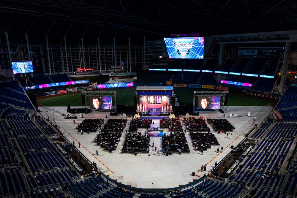 On-field conference setup with stadium videoboards and stage lighting.