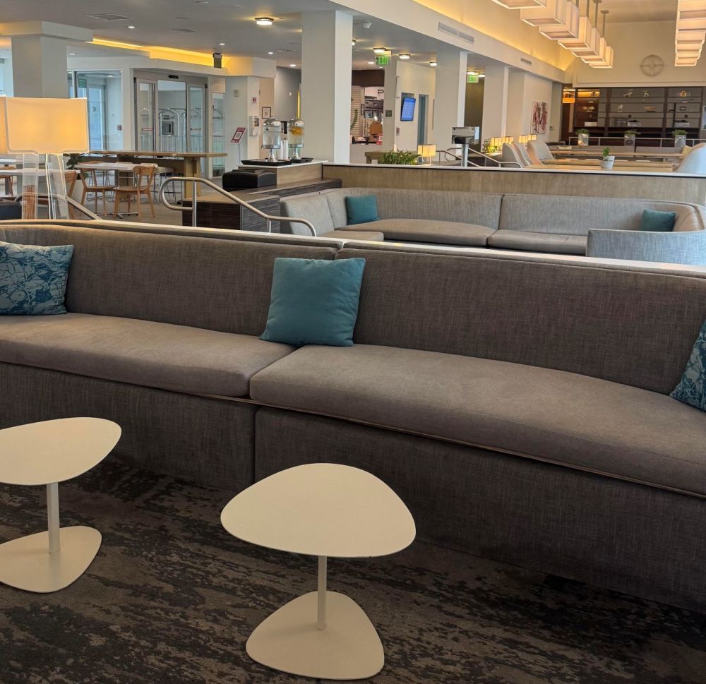 A spacious and modern lobby, featuring plush sectional seating accented with vibrant teal throw pillows and sleek white coffee tables.