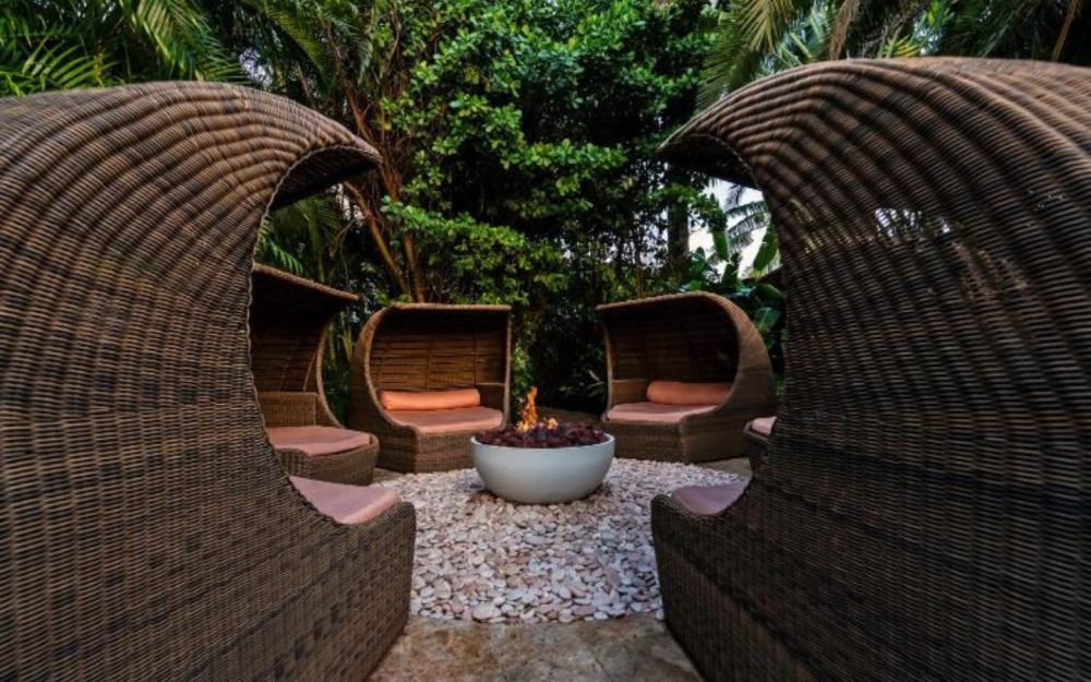 Fire pit seating area surrounded by lush tropical landscaping at The Standard Spa, Miami Beach, featuring woven lounge chairs and an intimate outdoor