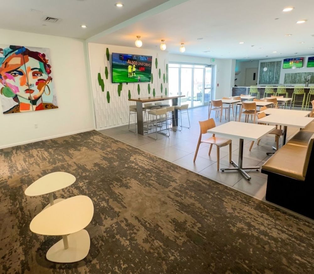 This bright and modern lounge with raised bar counter with high-backed bar stools with lime-green seats, and a flat-screen TV to display sports media.