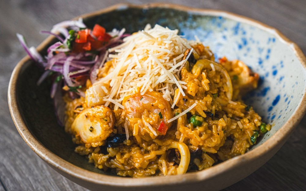Typical Peruvian creamy seafood rice sautéed with white wine and topped with Parmesan cheese, served with “sarza criolla”