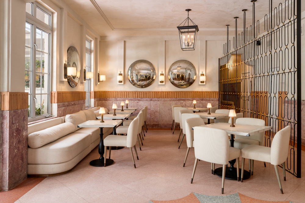 Elegant hotel lounge with soft neutral seating, marble tables, warm lighting, arched mirrors, and refined Art Deco–inspired details.