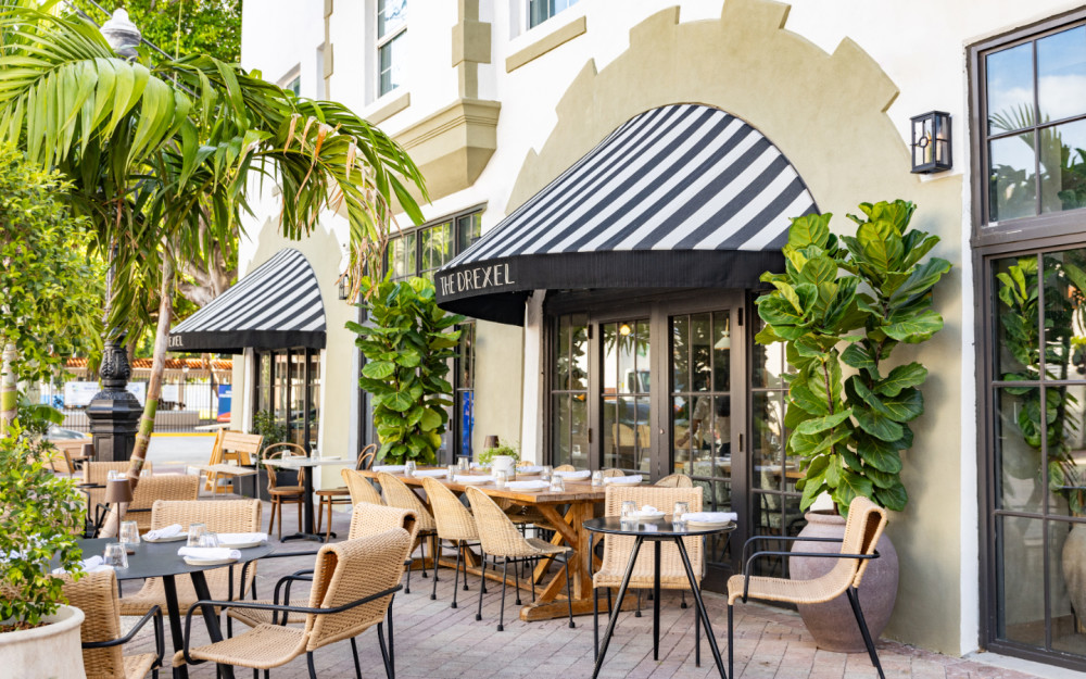 Chic outdoor dining at The Drexel—striped awnings, lush greenery, and coastal charm on Miami Beach’s iconic Española Way.