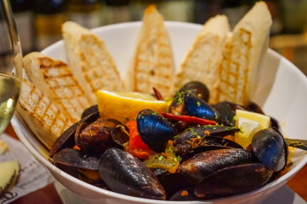 Steamed Mussels: Fresh mussels steamed with white wine and onions; served with a light spicy tomato broth, chorizo, and toasted baguette bread.