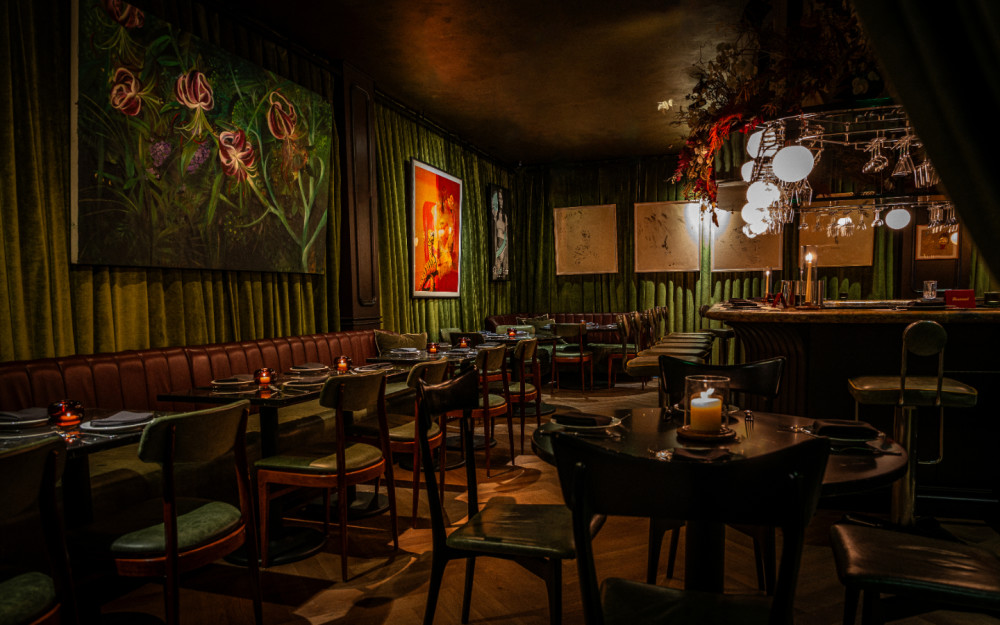 Tucked behind emerald drapery and curated canvases, this intimate dining room blends old-world charm with modern edge.