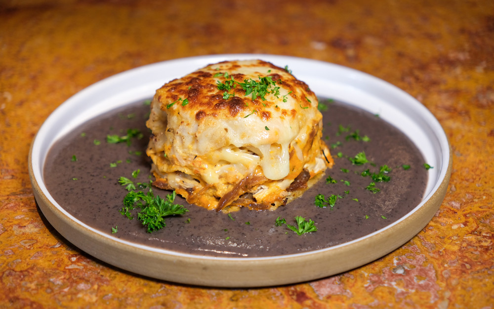Mexican Lasagna: Tortillas layered with cheese, shredded chicken, cream, and red ranchera sauce served over black bean purée.