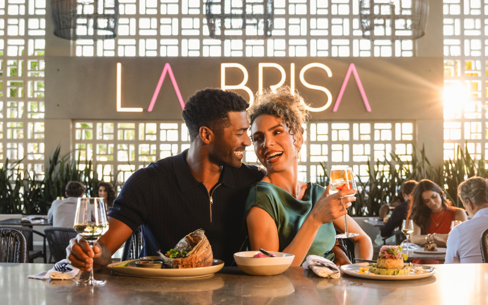 一对时尚的夫妇在 La Brisa 餐厅享用饮料和精美的菜肴，这是一家现代拉丁餐厅 Fusion 餐厅氛围充满活力，夕阳西下。