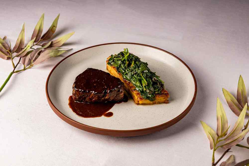 Prime Beef Tenderloin—elegantly paired with black truffle bread pudding, sautéed spinach, and a bold mustard jus for a rich, refined finish.