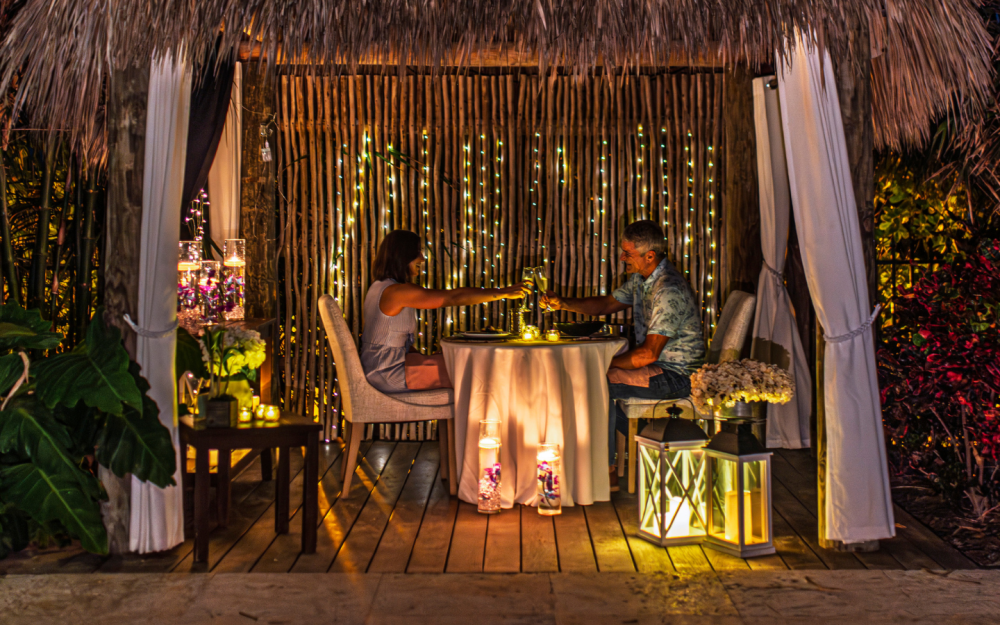 A candlelit private cabana dinner set beneath the palms, offering an intimate, romantic setting surrounded by lush gardens and warm tropical ambiance.