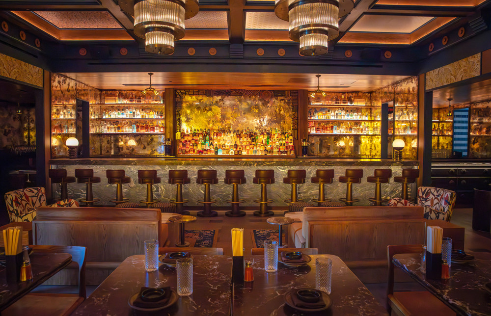 Interior view of Double Knot Miami’s Wynwood cocktail lounge: marble bar with stools, illuminated backlit spirits display and intimate dining tables.
