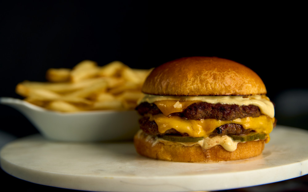 Two patties, melted cheese, crisp pickles, and a creamy sauce—stacked just right. Served with golden fries on the side. Simple. Always satisfying.