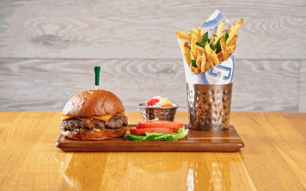 Unleash flavor with the Corsair Cheeseburger: 8oz blend, garlic pickle, spicy aioli, cheddar, herb fries.