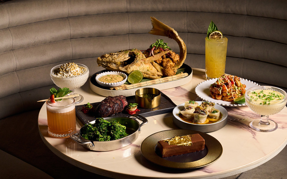 A whole fried fish served with fresh lime and dipping sauces, surrounded by a selection of Giselle Miami dishes and signature cocktails