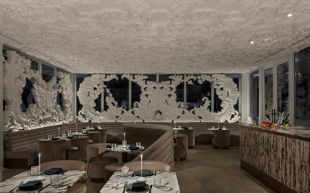 Giselle Miami’s elegant dining room features sculptural white artwork, curved seating and marble tables in a sophisticated, intimate setting