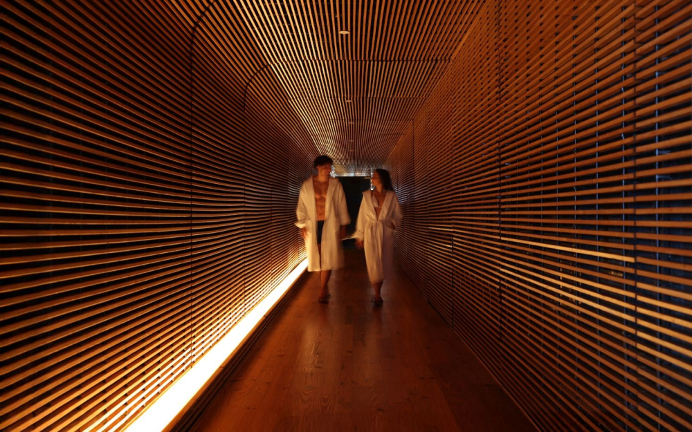 Spa corridor at The Standard Spa, Miami Beach, featuring warm wood slat walls and guests in robes walking through the hotel’s wellness facilities.