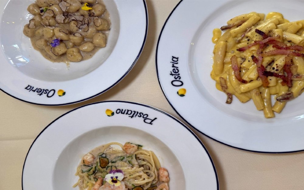 Three гурман Pasta тарелки: трюфельные ньокки, карбонара и спагетти с креветками, подаваемые на элегантных тарелках от Osteria Позитано.