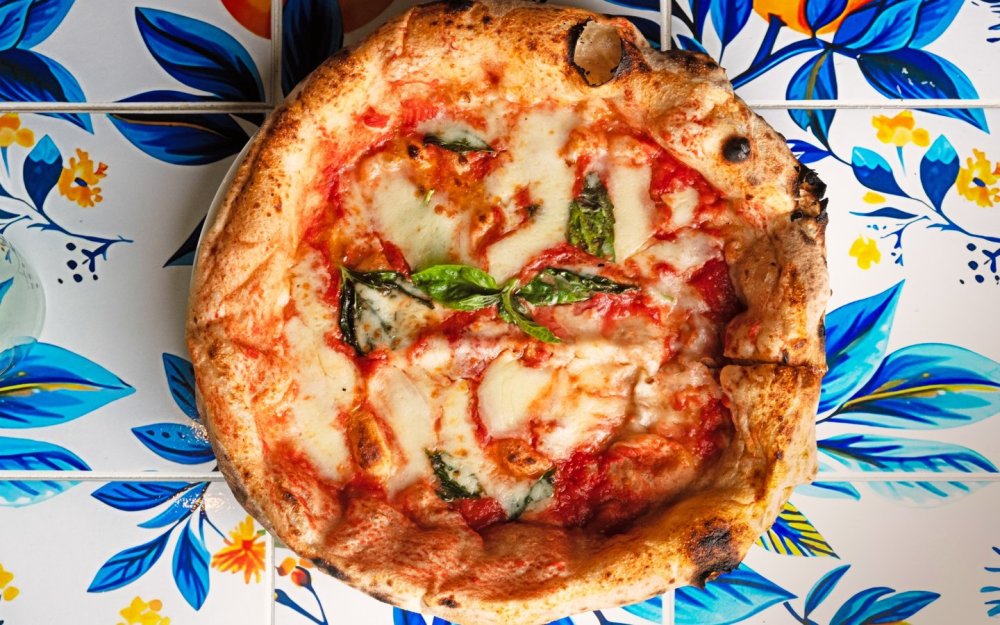 Neapolitan-style Margherita pizza with fresh mozzarella, tomato sauce, and basil, served on a vibrant ceramic-tiled table.