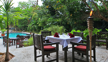 Dine under the leafy palm trees by the pool with tikki torches surrounding the property at sunset every evening.