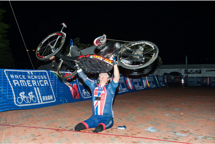 a para cyclist without legs, holds his bike over his head at the Annapolis, MD Finish line