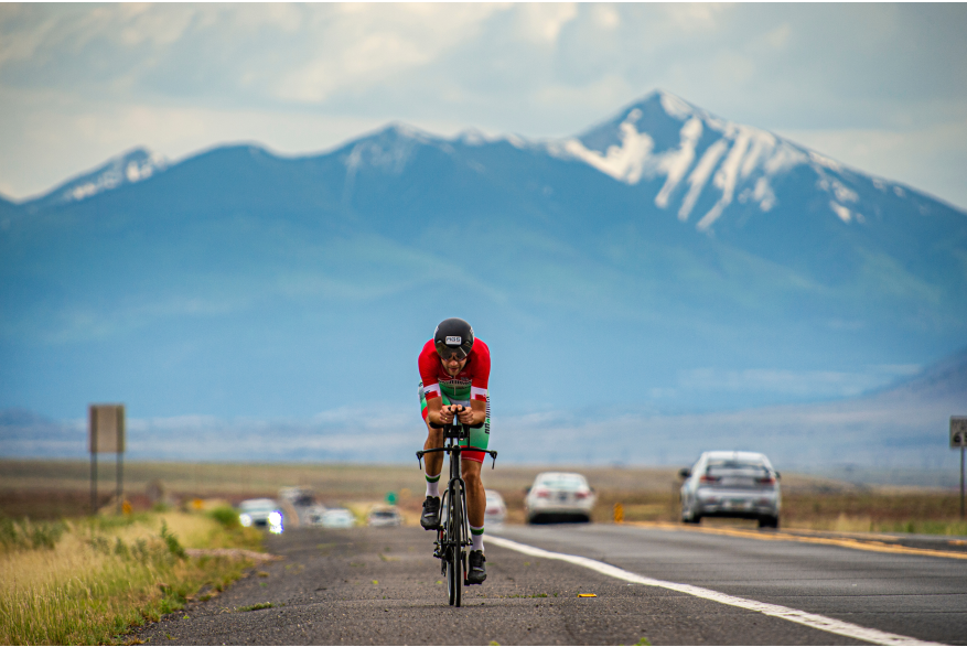 a man rides his bicycle down a long road with snow capped mountains in the background