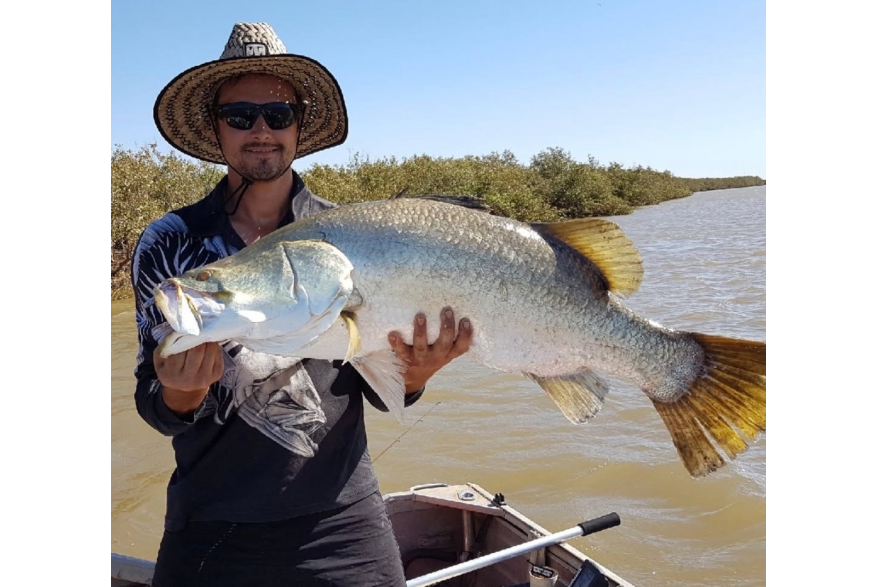 A man in a tinny holding a freshly caught barra, in a creek near Port Hedland