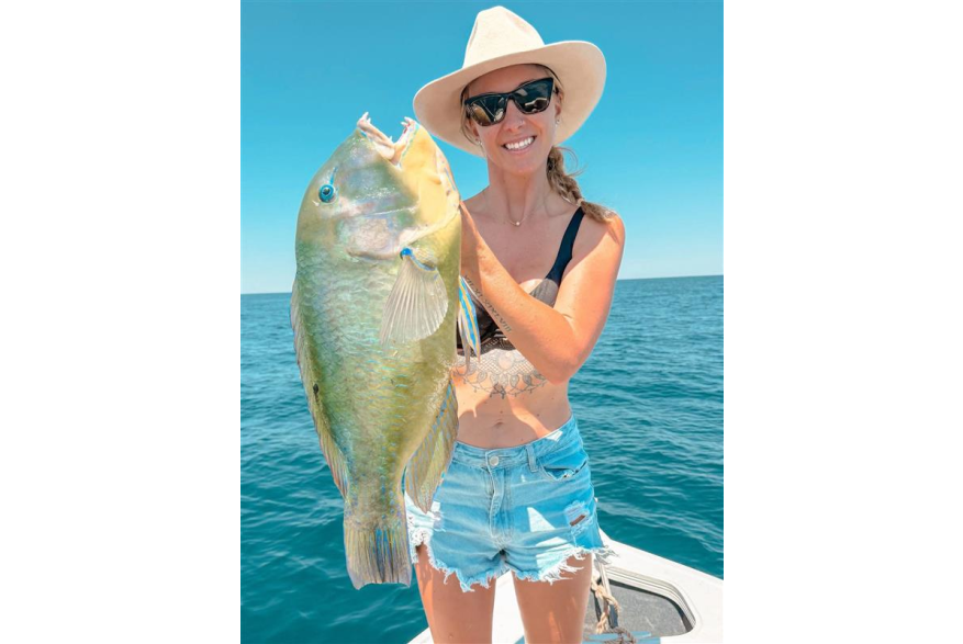 A woman in a boat holding a freshly caught Bluebone fish, in the waters off Port Hedland