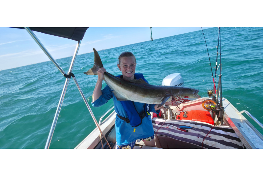 A woman in a boat holding a freshly caught cobia fish, in the waters off Port Hedland