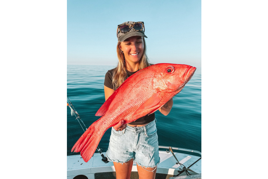 A woman in a boat holding a freshly caught Red Emporer