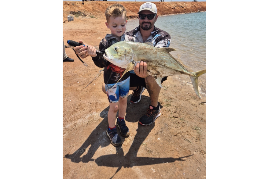 A child holding a Trevally, freshly caught from the shore at Port Hedland. A man crouches behind the child, supporting him