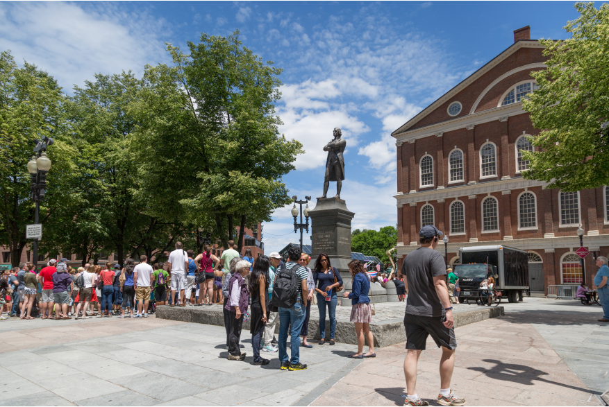 A group of visitors pause at the Samuel Adams statue outside Faneuil Hall