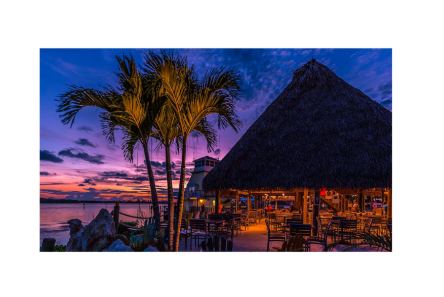 Night shot of palm trees and tiki bar with sunset in the background at Lighthouse Grill at Stump Pass in Englewood Florida