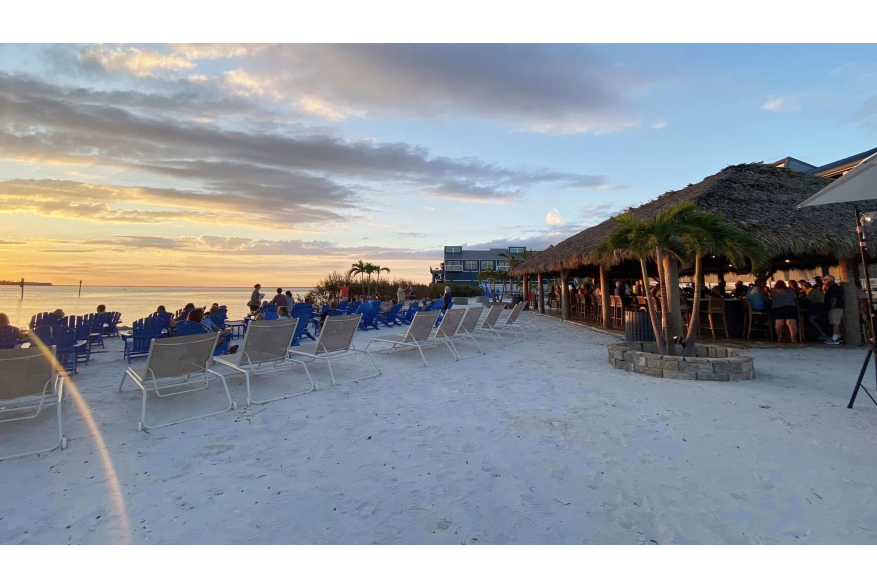 Sunset Beach Club view of dry beach, tiki hut, water, and sunset