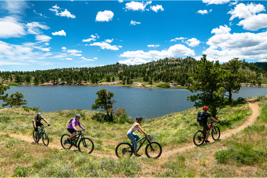 Four people riding mountain bikes around a lake