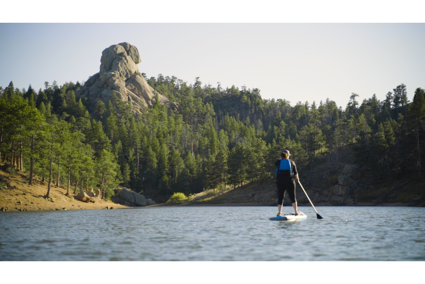 Lady standing up on paddlebaord holding an oar floating on a crystal blue lake.