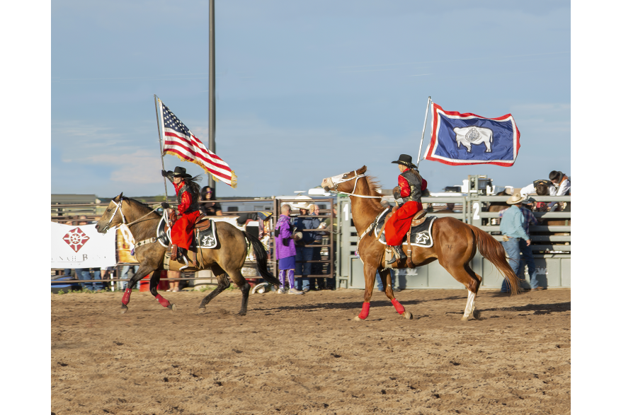 Two horse back riders post the colors at a rodeo