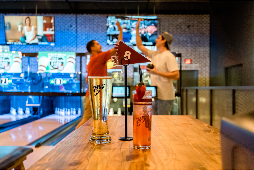 two guys high-fiving in a blowline alley with drinks in the foreground