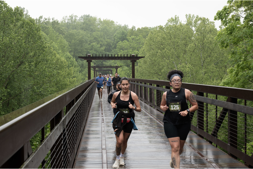 runners racing across a greenway bridge in the rain