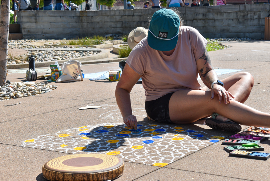woman creating a large chalk graphic on a sidewalk
